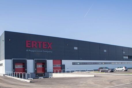 The Ertex warehouse, a Peppermint Company, features loading docks and parked cars under a clear blue sky.