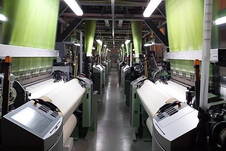 In einer modernen Weberei produzieren Maschinen grüne Textilbahnen in einem industriellen Fertigungsprozess.