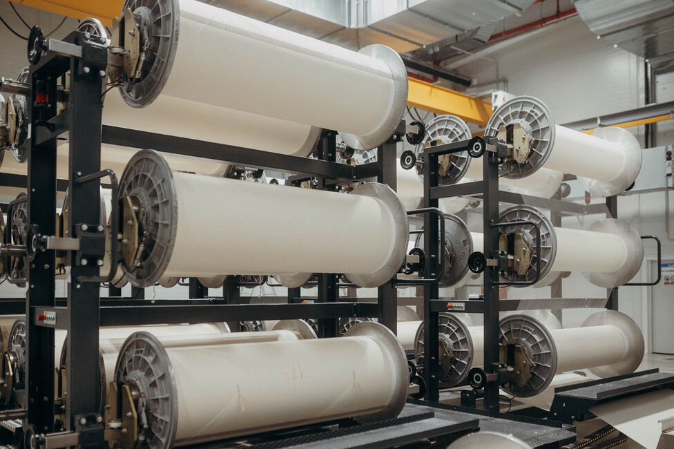 Rulouri mari de material textil sunt depozitate pe un suport metalic într-o fabrică modernă de textile Ertex International.