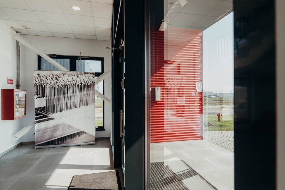 Un interior modern cu un panou alb-negru și o ușă de sticlă reflectând lumină în clădirea Ertex International.