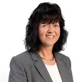 A woman in a gray blazer smiles confidently against a plain white background.
