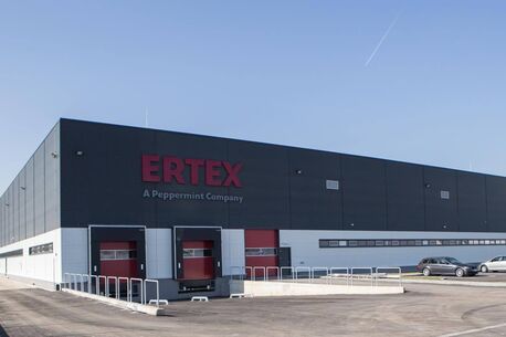 Ein modernes Industriegebäude mit dem Logo "ERTEX" steht unter einem klaren blauen Himmel.