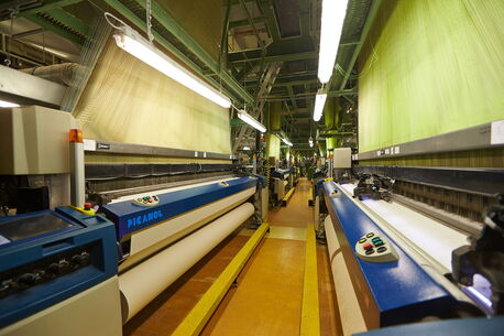 A textile factory features advanced weaving machines with vibrant green threads, showcasing industrial efficiency.